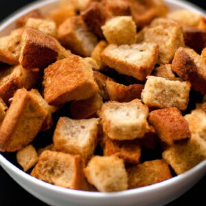 Imagem de deliciosos croutons dourados e crocantes feitos na Airfryer. Os croutons são feitos com pão cortado em cubos temperado com azeite, sal e pimenta. Eles são cozidos na Airfryer até ficarem dourados e crocantes. Os croutons são um ótimo complemento para saladas, sopas e ensopados.