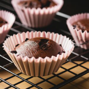 Imagem de cupcakes de chocolate assados em forminhas de papel dentro da cesta da Airfryer. Os cupcakes são cobertos com uma cobertura de chocolate cremosa e polvilhados com granulado de chocolate.