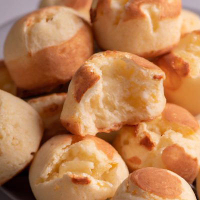 Imagem mostrando um bolo de pão de queijo dourado e recém-assado em uma Airfryer, cercado por ingredientes como polvilho azedo, queijo parmesão e ovos.