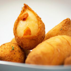 Imagem de uma coxinha de frango com batata frita na airfryer. A coxinha é dourada e crocante, com pedaços de frango e batata visíveis. A batata frita é fina e crocante, com uma cor dourada.