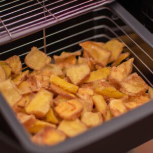 Imagem de salgadinhos de batata-doce crocantes e dourados preparados na Airfryer, servidos em uma tigela com um molho ao lado.