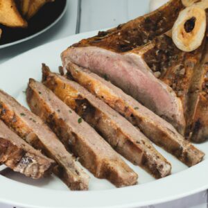 Imagem de uma grelha de ar com um bife T-bone suculento e grelhado no interior. O bife é perfeitamente cozido, com marcas de grelha douradas na superfície. Ele é guarnecido com alecrim fresco e fatias de limão.