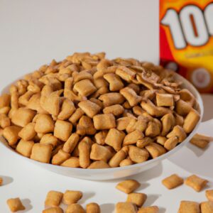 Barrinhas de cereal crocantes e douradas feitas na Airfryer. As barrinhas são cortadas em pedaços quadrados, revelando seu interior dourado e crocante. O fundo da imagem mostra a Airfryer usada para fazer as barrinhas, com sua cesta de cozimento removível.