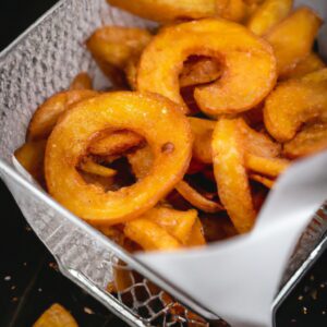 Foto de batatas doces cortadas em fatias grossas e fritas em uma Airfryer. As batatas são douradas e crocantes, com uma polpa macia e amanteigada no interior. Elas são temperadas com sal, pimenta e páprica, e servidas com um molho de iogurte grego.