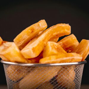Batata-doce rústica crocante e dourada, assada na Airfryer. A casca enrugada exibe um tom marrom-avermelhado, contrastando com a polpa laranja vibrante no interior. As bordas das fatias são ligeiramente enroladas, criando uma textura crocante e convidativa.