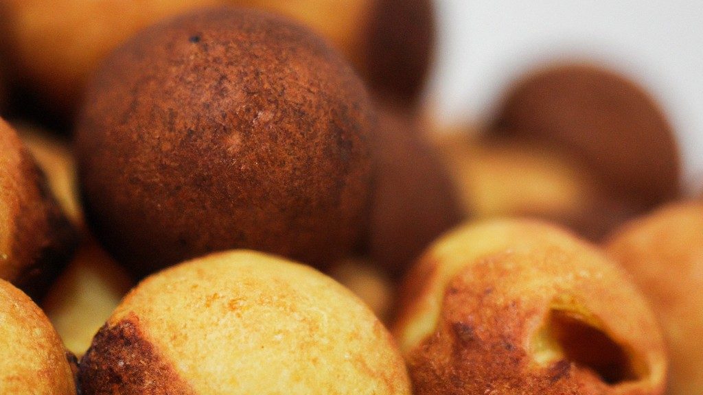 Imagem de bolinhos de chuva fritos na airfryer, dourados e crocantes, polvilhados com açúcar de confeiteiro. Eles são servidos em um prato branco com uma tigela de calda de açúcar ao lado.