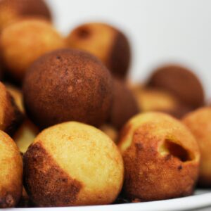 Imagem de bolinhos de chuva fritos na airfryer, dourados e crocantes, polvilhados com açúcar de confeiteiro. Eles são servidos em um prato branco com uma tigela de calda de açúcar ao lado.