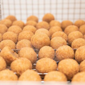 Imagem de bolinhos crocantes e dourados de feijoada, feitos na Airfryer. Os bolinhos são recheados com uma mistura saborosa de feijão preto, carne de porco e temperos, e são servidos com um molho de pimenta saboroso.