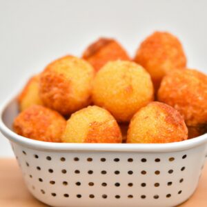 Imagem de bolinhos dourados e crocantes em forma de bola, feitos com risoto restante e revestidos com farinha de rosca. Os bolinhos são servidos em um prato branco com um molho de tomate ao lado.