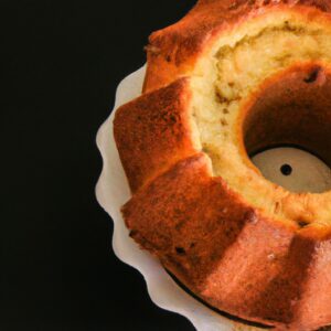 Imagem de um bolo redondo e dourado cozido em uma airfryer. O bolo é coberto com uma cobertura de chocolate e granulado colorido.
