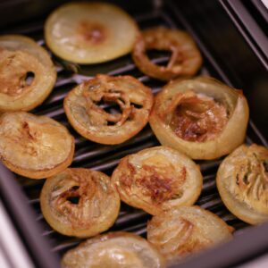 Imagem de uma cebola assada na Airfryer. A cebola é marrom-dourada e tem uma textura crocante. É cortada em rodelas e colocada numa travessa.