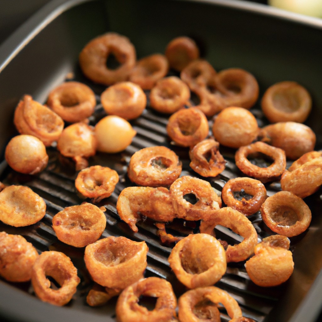 Imagem de cebolas caramelizadas crocantes e douradas preparadas na Airfryer. As cebolas são cortadas em fatias finas e caramelizadas até ficarem macias e ligeiramente crocantes. Elas têm uma cor marrom-dourada escura e são polvilhadas com ervas frescas para adicionar sabor. A imagem mostra o processo de cozimento das cebolas na Airfryer, com as fatias de cebola espalhadas na cesta da fritadeira.