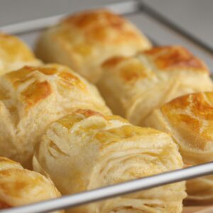 Fotografia de uma cesta de Airfryer contendo um queijo dinamarquês assado. O pão é dourado e escamoso, com uma cobertura de queijo cremoso e crocante. O queijo dinamarquês é polvilhado com açúcar de confeiteiro e servido com amoras frescas.