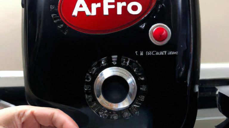 Imagem mostrando uma airfryer branca e cinza com uma cesta removível. A airfryer está sobre uma superfície de cozinha branca com utensílios de cozinha e ingredientes ao redor. O texto 