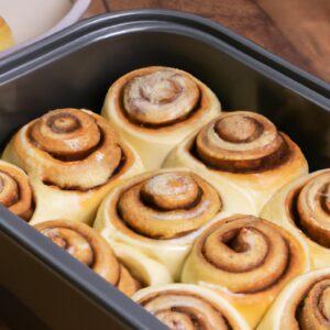Imagem mostra uma cesta de fritadeira cheia de rolinhos de canela dourados e crocantes, polvilhados com uma generosa camada de cobertura de cream cheese. Os rolinhos são macios e fofos por dentro, com um aroma doce e irresistível.
