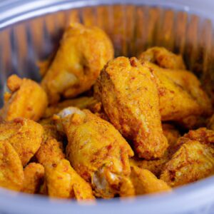 Imagem de uma sobrecoxa de frango crocante e suculenta cozida em uma Airfryer, coberta por um tempero dourado e servida em um prato com guarnições de batata frita e vegetais.
