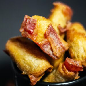 Imagem de torresmo crocante e dourado, preparado na airfryer. O torresmo é cortado em tiras e disposto em uma cesta de arame da airfryer. O fundo da imagem mostra a airfryer, com a luz indicadora de aquecimento acesa.