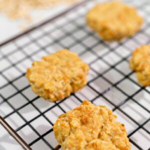 Imagem de cookies de banana e aveia dourados e crocantes dispostos em uma cesta de arame. Os cookies são feitos com uma mistura de aveia, purê de banana, farinha de trigo integral e especiarias, resultando em uma textura macia e mastigável com um sabor doce e frutado.