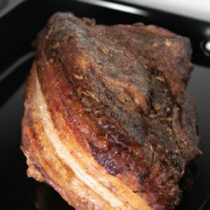 Imagem de uma costela bovina assada no bafo na Airfryer. A costela é suculenta e macia, com uma crosta crocante e dourada. É guarnecida com ervas frescas e fatias de limão.