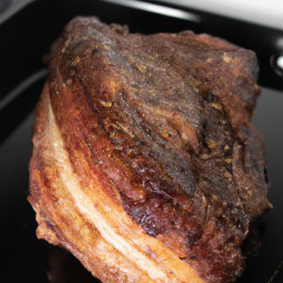 Imagem de uma costela bovina assada no bafo na Airfryer. A costela é suculenta e macia, com uma crosta crocante e dourada. É guarnecida com ervas frescas e fatias de limão.