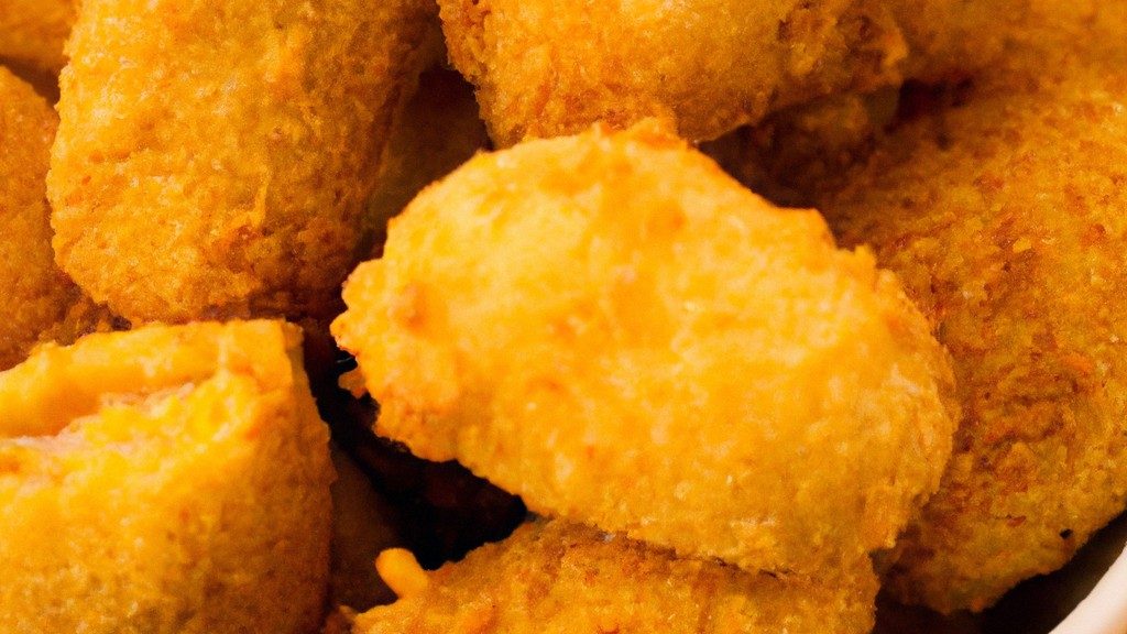 Uma foto de cima para baixo de um croquete de milho recheado com frango, coberto com uma crosta crocante e dourada, servido em uma cesta de vime em uma superfície de madeira.