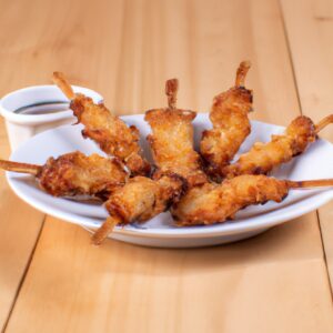 Imagem de espetinhos de frango empanados crocantes e dourados cozidos em uma airfryer. Os espetinhos são apresentados em uma cesta de metal, rodeados por migalhas de pão crocantes.