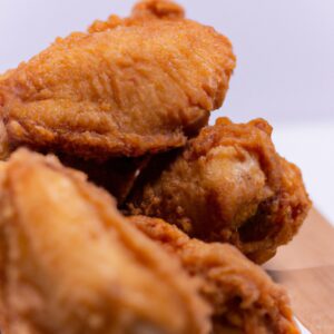 Imagem de filés de frango dourados e crocantes cozidos em uma air fryer. Os filés são servidos em um prato com um lado de legumes grelhados. O fundo é uma superfície de madeira escura.
