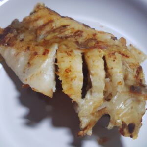 Imagem de filé de peixe grelhado frito na airfryer, servido com limão e ervas frescas. O peixe é dourado e crocante por fora, e branco e escamoso por dentro.