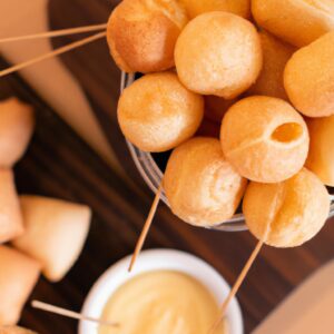 Imagem de uma Airfryer com uma cesta contendo uma panela de fondue de queijo quente e borbulhante. Ao lado da panela, há uma variedade de itens para mergulhar, como pedaços de pão, vegetais crus, frutas e chocolates. O fundo da imagem é uma mesa de madeira com uma toalha de mesa xadrez vermelha e branca. O texto na imagem diz "Fondue Completo Na Airfryer - Salgado E Doce".