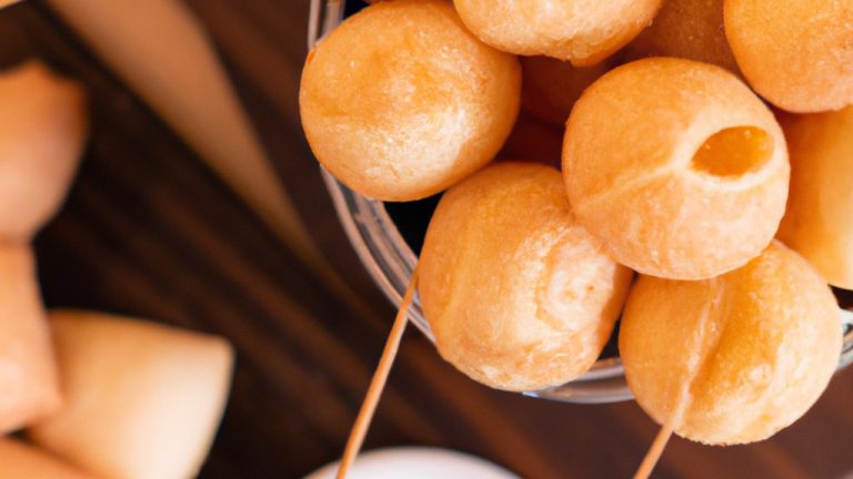 Imagem de uma Airfryer com uma cesta contendo uma panela de fondue de queijo quente e borbulhante. Ao lado da panela, há uma variedade de itens para mergulhar, como pedaços de pão, vegetais crus, frutas e chocolates. O fundo da imagem é uma mesa de madeira com uma toalha de mesa xadrez vermelha e branca. O texto na imagem diz 