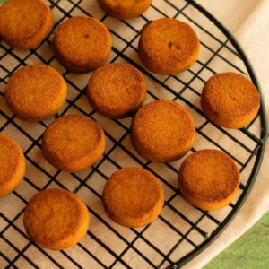 Imagem de biscoitos de gengibre dourados e crocantes, dispostos em uma cesta de arame sobre uma toalha de cozinha listrada. Os biscoitos têm formatos festivos, como homens de gengibre, estrelas e árvores de Natal. Os biscoitos estão quentes e fumegantes, tendo acabado de ser retirados da airfryer.
