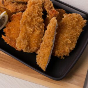 Imagem mostra lombinho empanado frito na airfryer, cortado em tiras finas e douradas, com uma crosta crocante e uma carne macia e suculenta no interior. O prato é servido com um molho cremoso ao lado, acompanhado de salada verde fresca.