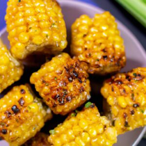 Uma fotografia de milho verde assado na airfryer. O milho é colocado em um prato branco e tem um tom dourado. As espigas de milho são polvilhadas com sal e pimenta e têm um aspecto crocante e delicioso.