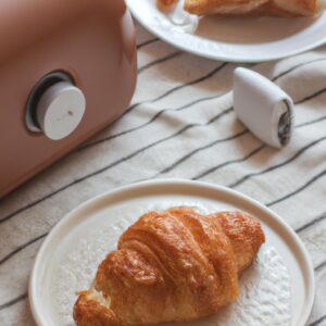 Imagem de mini croissants dourados e crocantes recém-saídos da airfryer, servidos em um prato branco com uma tigela de geléia de framboesa ao lado.
