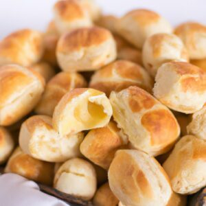 Pãezinhos caseiros recém-assados em uma airfryer, com uma crosta dourada e migalhos macios. Os pãezinhos são colocados em uma cesta de arame, prontos para serem servidos. O fundo é uma superfície de madeira com um pano de prato xadrez.