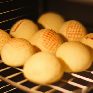 Pão de queijo crocante e dourado feito em uma Airfryer. Os pães de queijo são redondos e apresentam uma crosta exterior marrom-dourada, enquanto o interior é macio e arejado. Eles são servidos em um prato branco com uma tigela de molho de tomate ao lado.