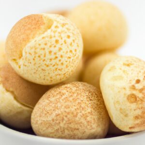 Foto de pães de queijo dourados e crocantes cozidos em uma airfryer, dispostos em um prato branco. Os pães de queijo têm um interior macio e aerado, e o exterior é crocante e dourado.