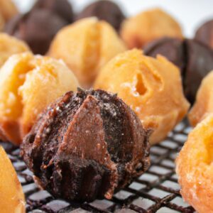 Imagem de um petit gateau de chocolate feito na Airfryer. O bolo é pequeno e redondo, com uma cobertura de chocolate derretido. O interior do bolo é úmido e cremoso, com um centro derretido. O bolo é servido em um prato branco com uma colher ao lado.