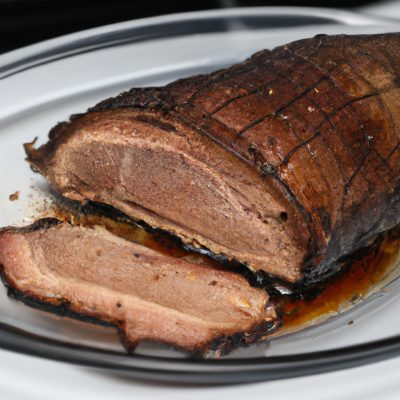 Imagem de uma picanha suína assada na Airfryer. A carne está dourada e suculenta, e é servida com uma salada de folhas verdes e um molho à parte.