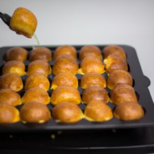 Imagem de uma queijadinha frita na Airfryer, com uma casca dourada e crocante e um recheio cremoso e macio. A queijadinha está em um prato azul, com uma colher ao lado.