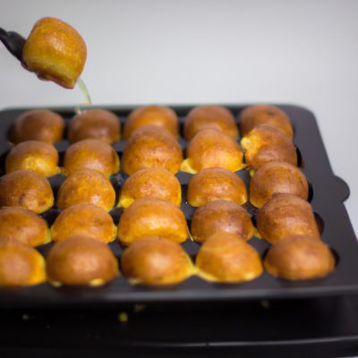 Imagem de uma queijadinha frita na Airfryer, com uma casca dourada e crocante e um recheio cremoso e macio. A queijadinha está em um prato azul, com uma colher ao lado.