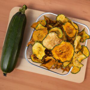 Imagem mostrando uma porção de chips de abobrinha dourados e crocantes preparados em uma airfryer. Eles são polvilhados com sal e pimenta e servidos em uma tigela branca.