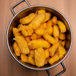 Foto de uma tigela de macaxeira frita, servida com molho à parte. A macaxeira é cortada em pedaços pequenos e frita até dourar. O molho é feito com tomate, cebola e pimentão.