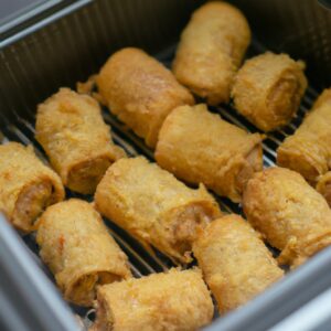 Imagem de um prato de rocambole de frango feito na Airfryer. O prato mostra um rocambole cortado em fatias, com recheio de espinafre e queijo derretido visível. A crosta externa do rocambole é dourada e crocante, e é guarnecida com tomate cereja e manjericão.