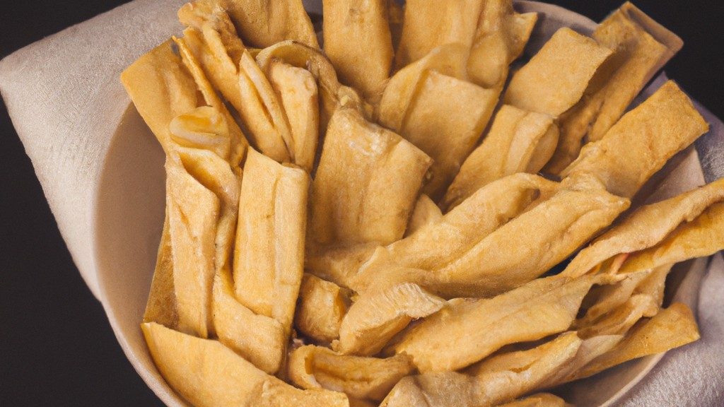 Imagem de uma cesta de airfryer cheia de tortilhas crocantes e douradas. As tortilhas são dobradas em quartos e estão empilhadas umas sobre as outras. A cesta está apoiada sobre uma superfície de madeira.