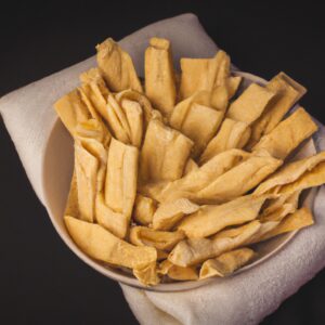 Imagem de uma cesta de airfryer cheia de tortilhas crocantes e douradas. As tortilhas são dobradas em quartos e estão empilhadas umas sobre as outras. A cesta está apoiada sobre uma superfície de madeira.