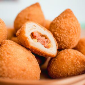 Imagem de coxinhas de asa douradas e crocantes cozidas em uma Airfryer, servidas em um prato com um molho de acompanhamento.